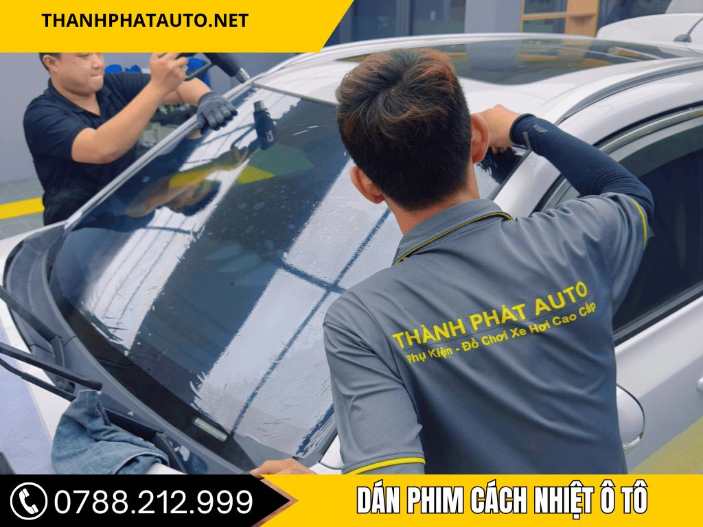 Hình ảnh kĩ thuật viên đang dán phim cách nhiệt ô tô được lắp đặt tại trung tâm phụ kiện ô tô tại Long An, hiển thị giao diện điều khiển hiện đại trong khoang nội thất xe.